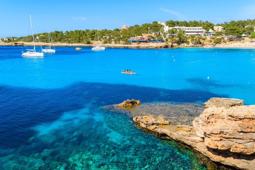 Tourists in kayak paddling on blue sea water of Cala Portinatx bay, Ibiza island