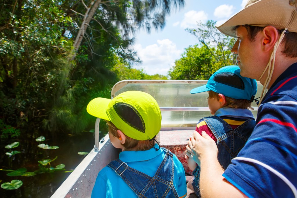 Two little kids boys and father enjoying air boat tour in Florida wetland swamp at Everglades National Park. Family, dad and children discovering wild nature and animals. Family having fun.